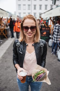 Beautiful young woman holding delicious organic salmon vegetarian burger and homebrewed IPA beer on open air beer an burger urban street food festival in Ljubljana, Slovenia
