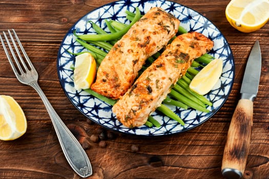 Baked or fried salmon fish with bush green beans on the plate.