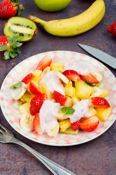Homemade sweet fruit salad of pineapple, strawberries, kiwi and yogurt on old rustic wooden table.
