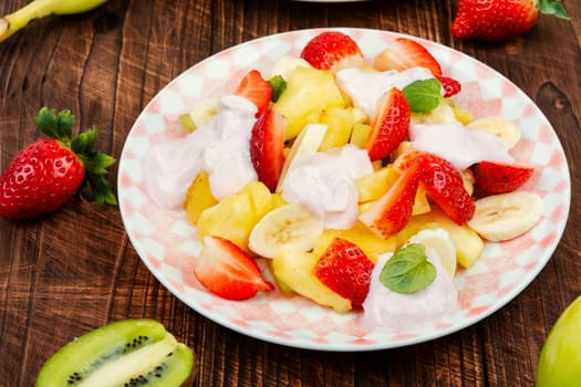 Homemade sweet fruit salad of pineapple, strawberries, kiwi and yogurt on old rustic wooden table.