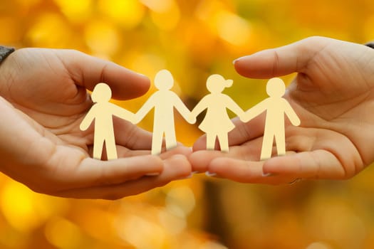Two hands delicately hold a paper cutout of a diverse family, symbolizing love and unity.