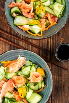 Homemade Asian salad with smoked salmon and fresh cucumber on old rustic wooden table. Flat lay.