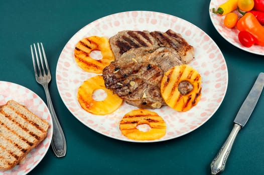 Tasty grilled meat,roasted with pineapple. Grilled steak and ananas on wooden table.