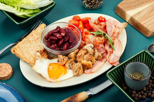 English breakfast: fried egg, roasted bacon,vegetables, beans and toast on a plate.