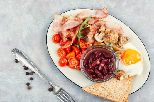 English breakfast: fried egg, roasted bacon,vegetables, beans and toast on a plate.