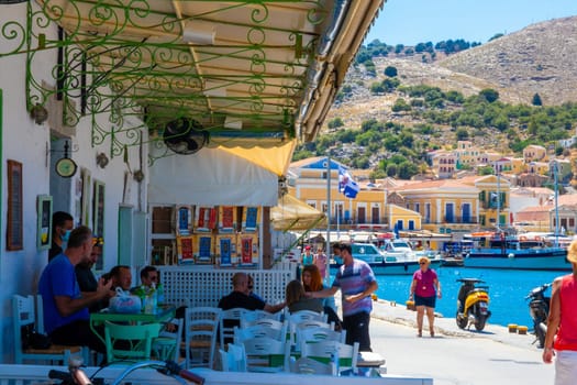 SYMI, Greece - Jun 03, 2021. A restaurant on the harbour promenade of Symi town where tourists linger. Most beautiful and romantic district in the whole Aegean.