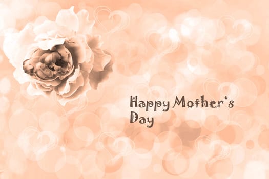 Happy Mothers Day Card. A champagne brown greeting card with an artificial rose flower and the text on an abstract bright blurred heart background.