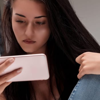 Young woman's gaze is fixed on her phone, reflecting a moment of personal reflection and digital interaction