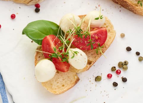 Round mozzarella, cherry tomatoes and microgreens on a piece of white bread, a healthy sandwich, top view