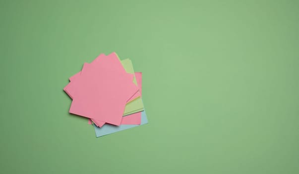 Stack of paper blank stickers on green background, top view. Copy space