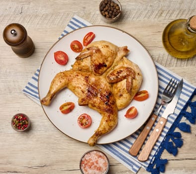 Whole fried chicken with spices in a white round plate on the table, top view