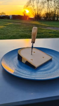 Blocks of hard cheese. Sliced cheese on cutting board in the background a beautiful sunset at the lake