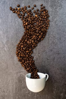 Spilled cup of coffee with roasted  beans forming like a smoke shape, vertical