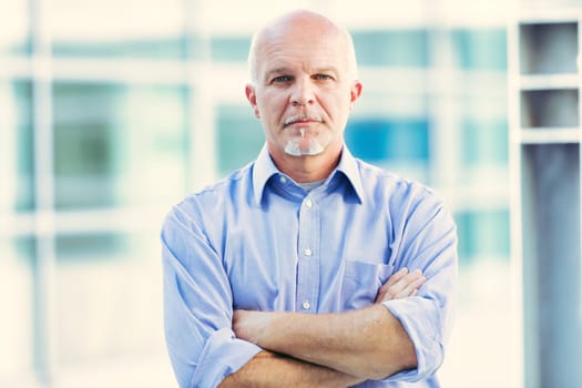 Senior professional stands confidently with arms crossed in front of a modern glass building, embodying seasoned leadership and expertise