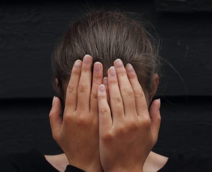 beautiful woman covering her face with her hands against black background