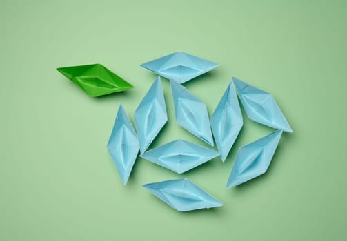 Group of blue paper boats heading in one direction and one green one heading in the opposite direction. The concept of individuality, uniqueness and talent of the employee. Get away from the influence