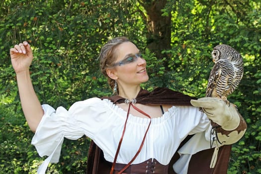 A woman, dressed as a medieval huntress, has a tawny owl on her hand