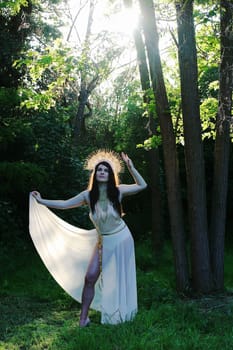 A woman as a goddess stands in the forest, backlit by the sun