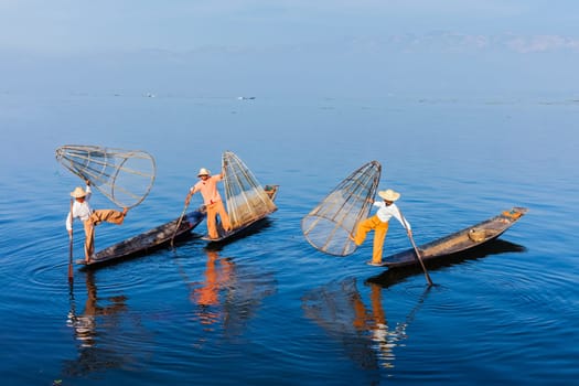 Myanmar travel attraction landmark - Traditional Burmese fishermen balancing with fishing net on boats at Inle lake in Myanmar. They are famous for their distinctive one legged rowing style.