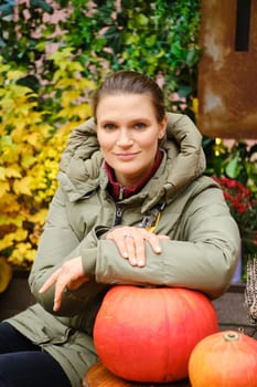 Lovely woman sitting at an autumn fair with her hand on a pumpkin on the table