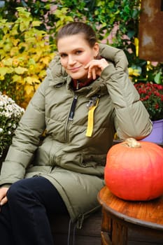 Smiling mid-aged woman in warm down jacket among autumn decoration