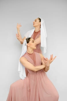 Two female dancers perform hand movements on grey background