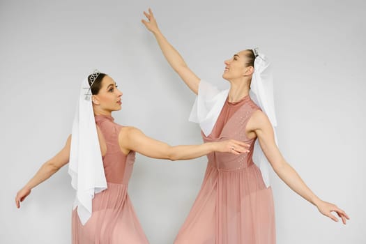 Two ballerinas in peach dress waving hands in front of each other on grey background