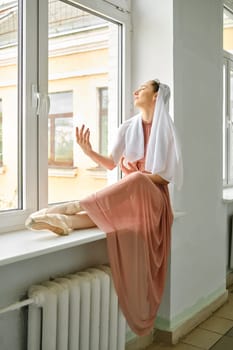A ballerina sits on the windowsill during a break and repeats the movements of her hands