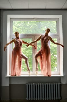 Silhouette of two ballerinas perform dance moves while standing on a windowsill in a hallway