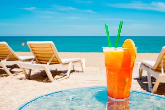 Orange cocktail or orange juice on a beach restaurant table against the background of the sea and sunbeds