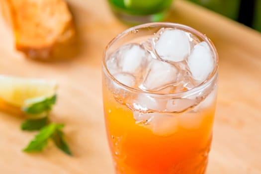 Glass with orange summer cocktail and ice cubes on table.