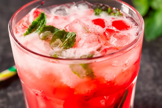 Glass of cold red summer fruit cocktail with mint leaves and ice cubes close up.