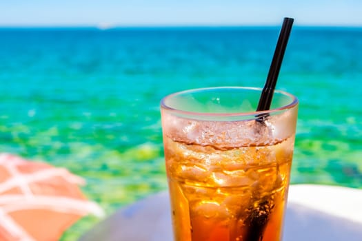 Glass with refreshing drink or iced tea in a glass against the background of the sea in summer.