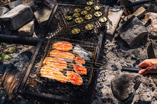 Salmon steaks and zucchini mugs grilled on a grill over a campfire during a picnic in the woods.