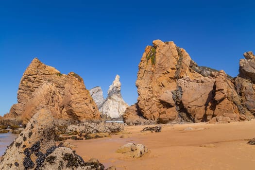 Towering rock cliffs at Praia Da Ursa Beach, Sintra, Portugal. Atlantic ocean waves and sandy beach near famous Cabo da Roca in Portugal