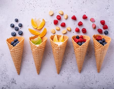 Waffle cones with different types of fruit on a light background