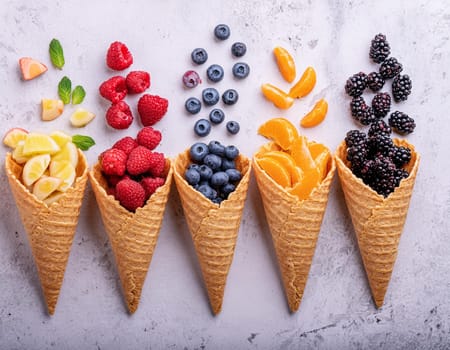 Waffle cones with different types of fruit on a light background