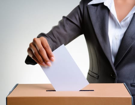 Ballot box with hand voting on a blank ballot paper against a light background.
