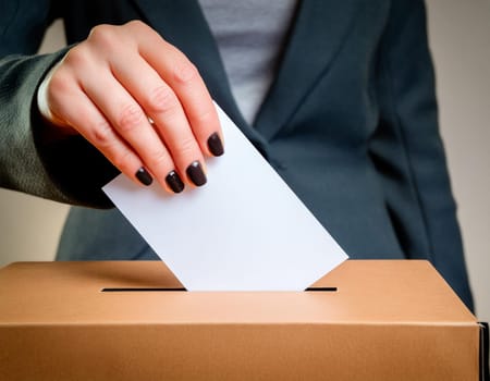 Ballot box with hand voting on a blank ballot paper against a light background.