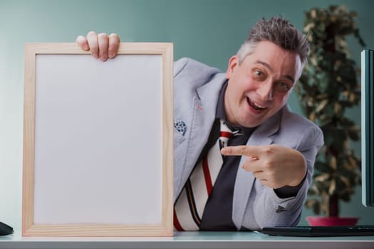 Cheerful businessman in a grey suit playfully points at a blank whiteboard, ready to present fresh ideas