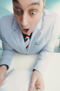 Shocked news anchor in a light grey suit leans forward with wide eyes, visibly startled by the document's contents