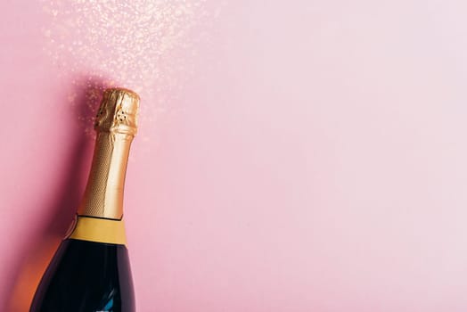 Champagne bottle with gold ribbon on pastel pink background with glitter. New year celebration banner design. Minimal flat lay christmas celebration border.