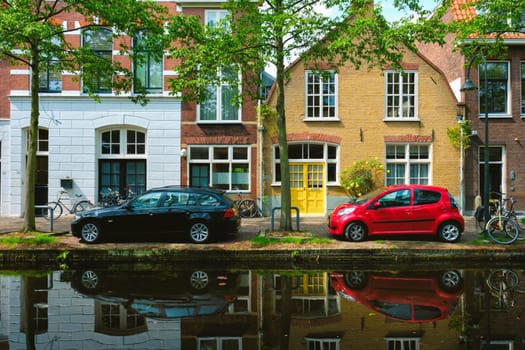Cars and bicycles on canal embankment in street of Delft with reflection. Delft, Netherlands