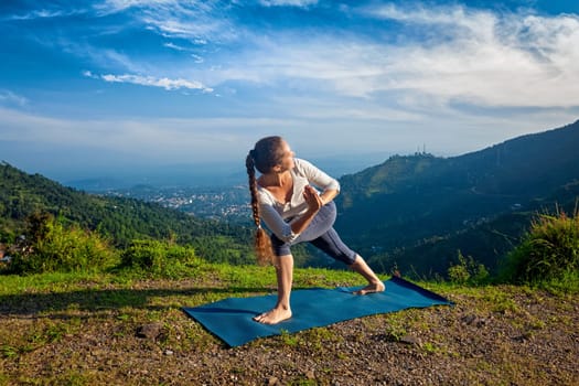 Woman practices Ashtanga Vinyasa yoga asana Utthita Parsvakonasana varitation - extended side angle pose outdoors in mountains in the morning