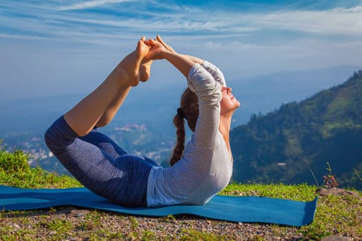 Yoga outdoors - young woman doing Ashtanga Vinyasa Yoga asana Dhanurasana - bow pose - in Himalayas mountains in the morning Himachal Pradesh, India