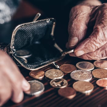 Detailed closeup photo of elderly 96 years old womans hands counting remaining coins from pension in her wallet after paying bills. Unsustainability of social transfers and pension system.