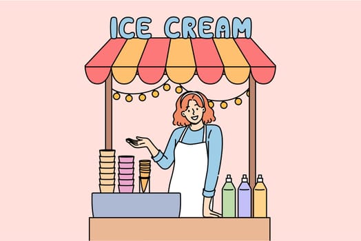 Woman sells ice cream in street stall and makes gesture inviting you to try cold dessert. Girl selling ice cream in waffle cones with addition of sweet syrups to quench summer thirst