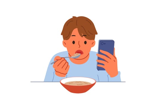 Boy suffering from digital addiction eats and watches video on mobile phone at same time. Schoolboy needs help of psychologist to combat addiction to phone and use of social networks