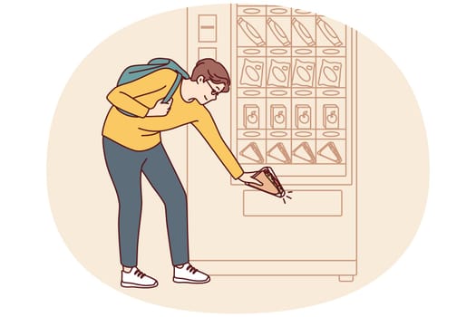 Man student bends down to pick up sandwich while shopping for lunchtime snack from vending machine. Shopper uses automatic vending machine to whet appetite after college or university classes
