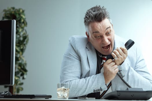 middle-aged man in a light suit and striped tie yells angrily into a phone, his expression intense and frustrated. Managing public relations appears challenging, with a glass of whiskey on the desk hi